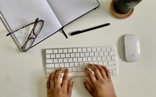 desk scene of hands typing at a keyboard