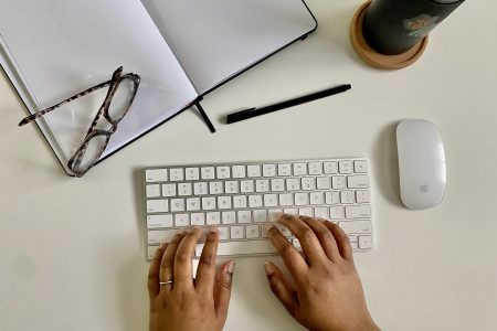 desk scene of hands typing at a keyboard